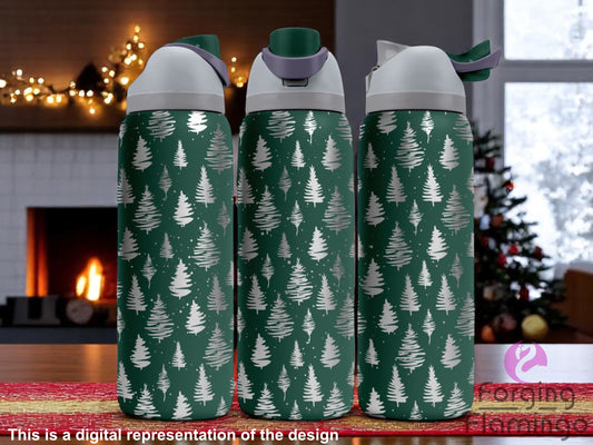 Three dark green Owala tumblers with laser-engraved Christmas tree patterns in various styles, displayed indoors on a festive table with a cozy fireplace and decorated Christmas tree in the background. Forging Flamingo logo appears in the bottom right corner.