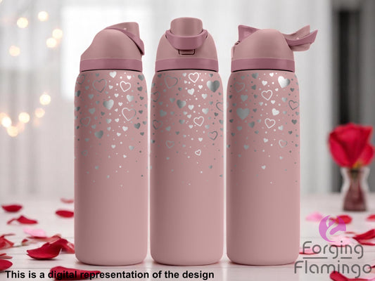 Three stainless steel tumblers with a soft pink coating, featuring a scattered laser-engraved heart pattern in various sizes concentrated toward the top and gradually fading downward. The tumblers are displayed on a light surface with rose petals, set against a softly blurred background with red roses and string lights. Text at the bottom reads “This is a digital representation of the design.”