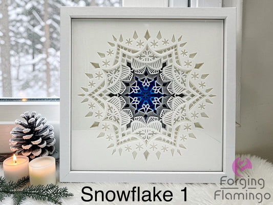 Framed snowflake art with blue center and geometric patterns, placed on a surface with candles and decorative items.