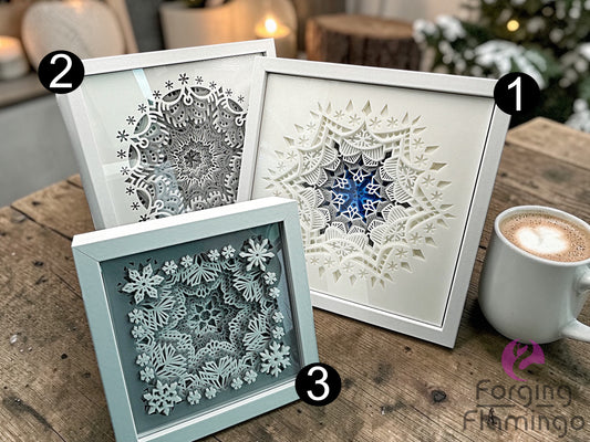 Three framed snowflake designs on a wooden surface with a cup of coffee.