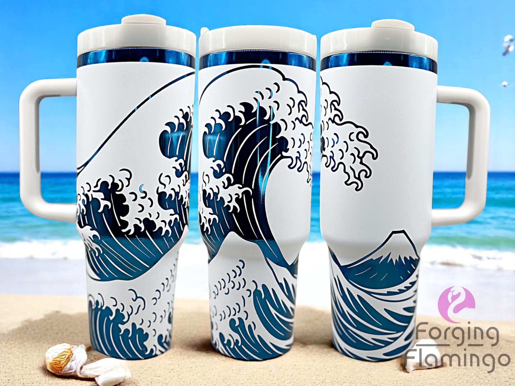 Three white handled tumblers with white lids displayed on a sandy beach background, featuring an engraved design inspired by The Great Wave off Kanagawa. The design wraps around the cups with deep blue wave details and Mount Fuji in the background, with a glossy metallic blue accent band near the top. The Forging Flamingo logo is visible in the lower right corner.
