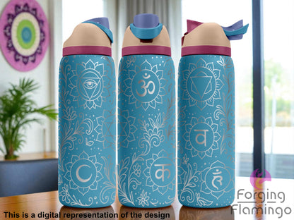 Three light blue Owala tumblers with laser-engraved chakra symbols and floral mandala patterns, including Om, third eye, root, and sacral symbols. Displayed indoors with natural light, a wooden table, and a colorful chakra tapestry in the background. Forging Flamingo logo appears in the bottom right corner.
