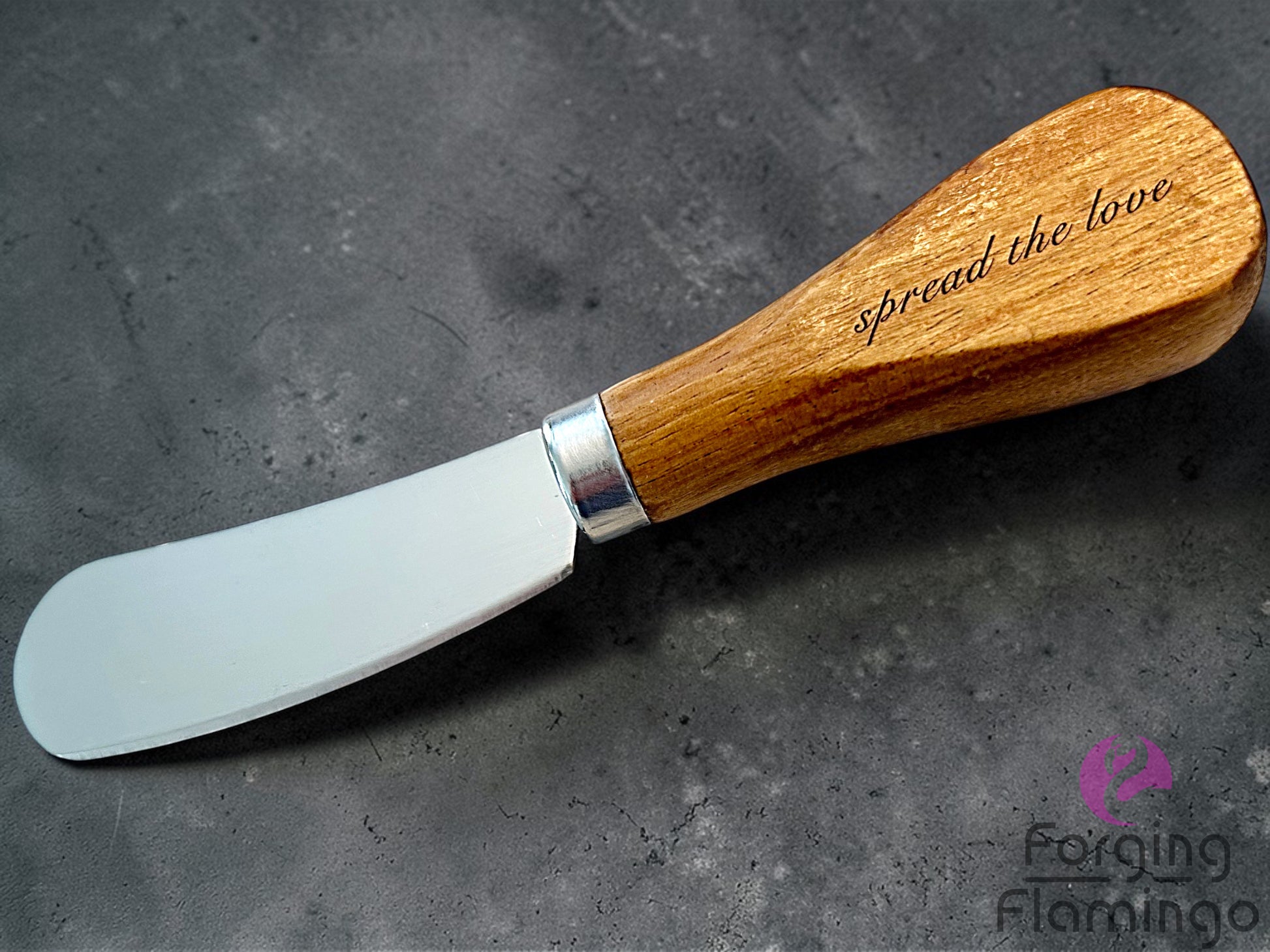 Butter knife with wooden handle and metal blade on a dark surface, engraved with 'spread the love'.