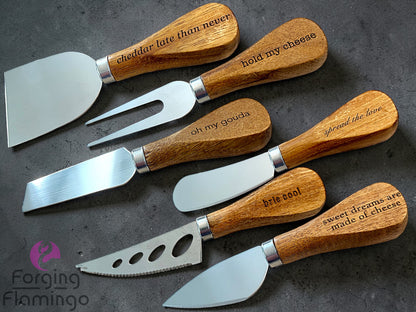 Set of cheese knives with wooden handles and engraved text on a dark surface, branded 'Forging Flamingo'.