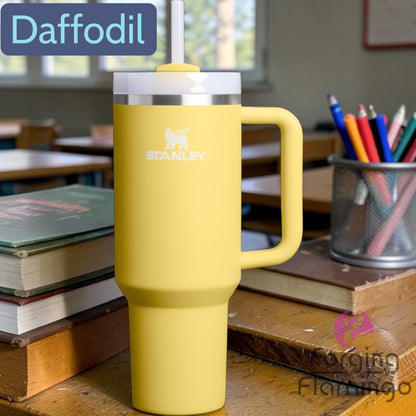 Yellow Stanley mug on a classroom desk with books and stationery.