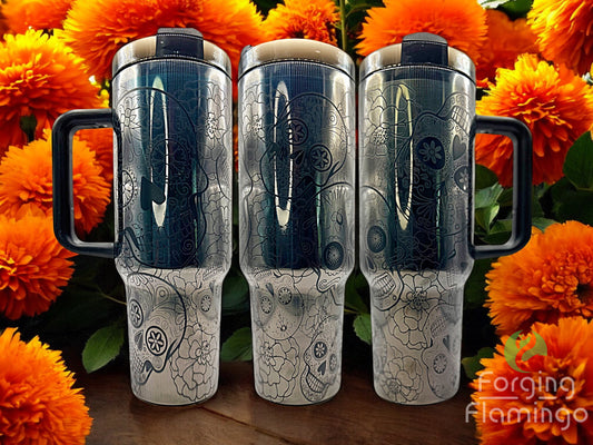 Three silver tumblers with black handles on a wooden surface with orange flowers in the background.