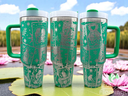 Three green laser-engraved tumblers featuring a seamless Frog Tarot card design, displayed outdoors on lily pads with pink lotus flowers and a bright blue sky in the background.