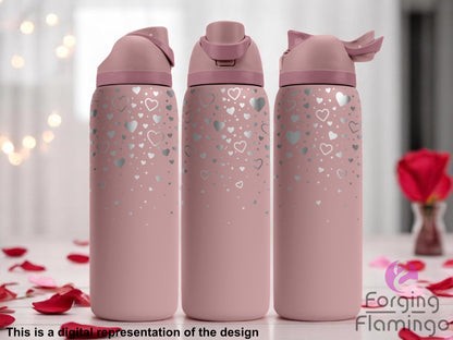 Three stainless steel tumblers with a soft pink coating, featuring a scattered laser-engraved heart pattern in various sizes concentrated toward the top and gradually fading downward. The tumblers are displayed on a light surface with rose petals, set against a softly blurred background with red roses and string lights. Text at the bottom reads “This is a digital representation of the design.”
