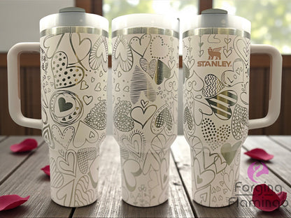 Three Stanley tumblers with decorative patterns on a wooden surface.