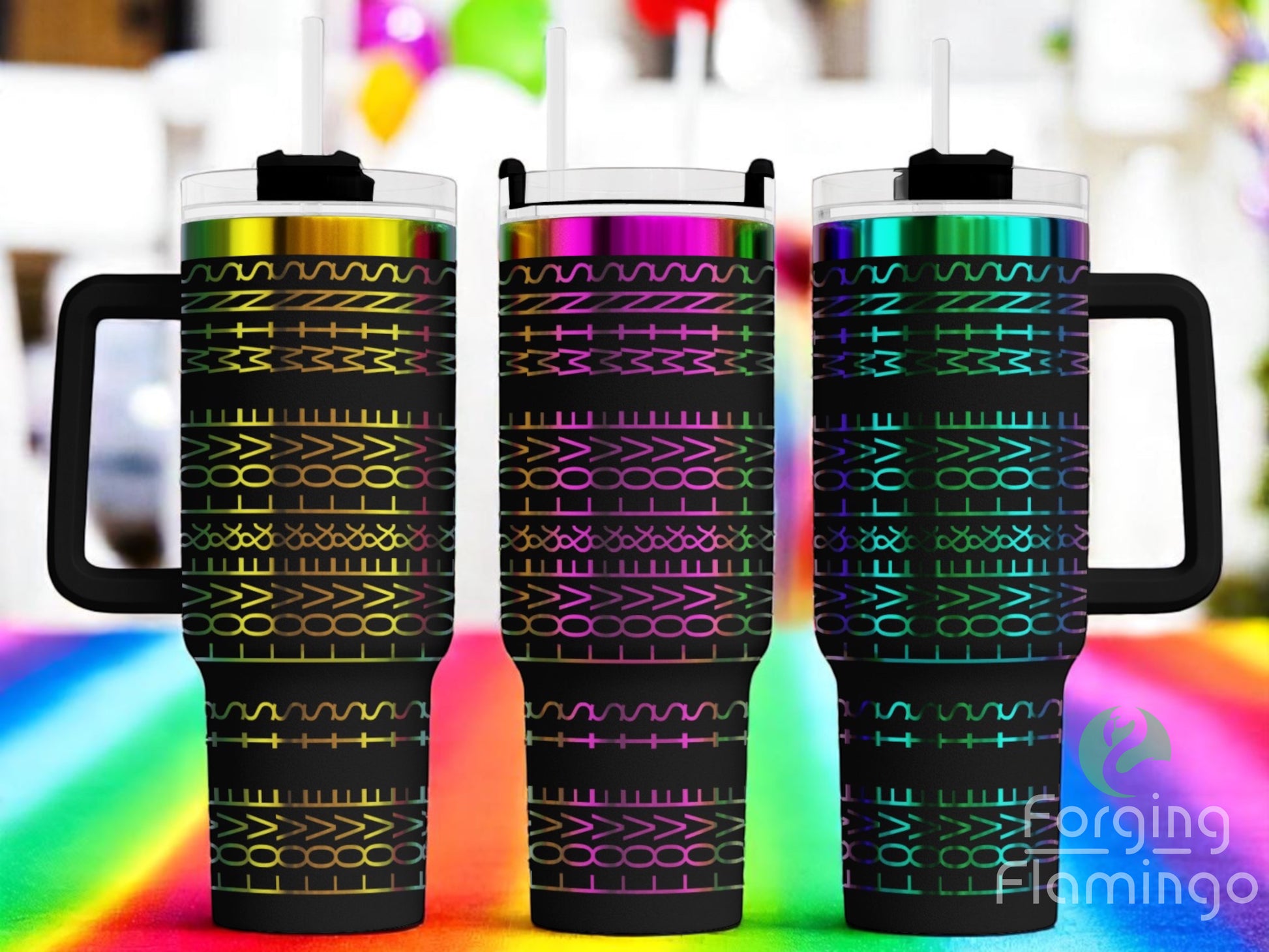 Three black tumblers with rainbow-gradient laser-engraved geometric patterns and “LOVE WINS” text, displayed upright with straws on a bright rainbow surface. Blurred festive balloons and decorations appear in the background. Forging Flamingo logo is visible in the bottom right corner.
