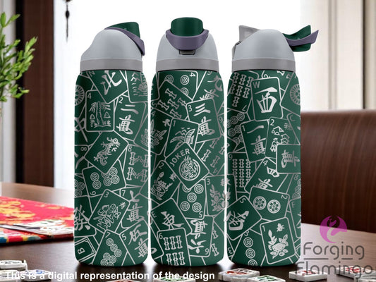 Three stainless steel tumblers with a dark green coating, featuring a laser-engraved wraparound pattern of scattered Mahjong tiles with intricate designs and Chinese characters. The tumblers are displayed on a tabletop surrounded by Mahjong game pieces in a casual indoor setting. Text at the bottom reads “This is a digital representation of the design.”
