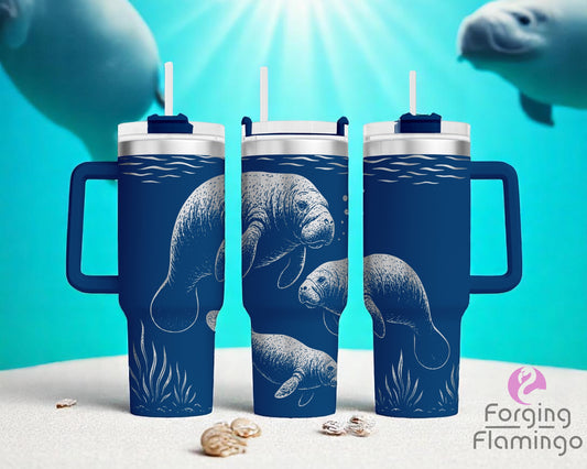 Three navy blue handled tumblers with white lids, displayed underwater. The tumblers feature an engraved design of manatees swimming among seaweed and bubbles. Each tumbler shows different angles of the manatees, with detailed engraving that reveals a shiny silver metal beneath the coating. The underwater background has a sandy ocean floor, light rays from above, and colorful coral in the distance. The Forging Flamingo logo is in the lower right corner.
