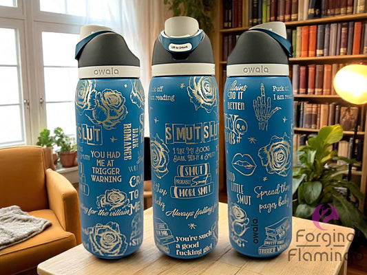 Three blue Owala tumblers with white laser-engraved dark romance and smut-themed quotes and rose illustrations, displayed in a cozy library setting with bookshelves, houseplants, and an orange armchair. Forging Flamingo logo appears in the bottom right corner.
