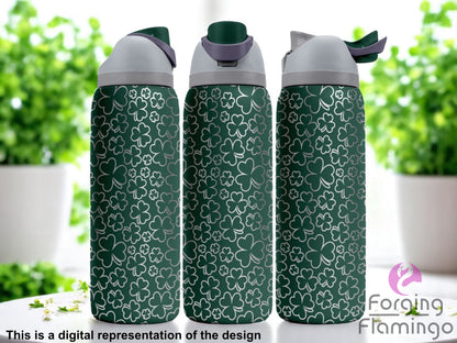 Three dark green Owala tumblers with a full-wrap laser-engraved shamrock pattern in various sizes, displayed indoors with bright natural light and leafy green plants in the background. Forging Flamingo logo appears in the bottom right corner.
