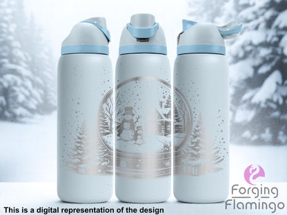 Three light blue tumblers with flip-top lids, engraved with a snow globe scene featuring a snowman, a child snowman, snowy pine trees, a cabin, and falling snow, displayed against a frosty winter background with snow-covered trees. Text below reads “This is a digital representation of the design.”
