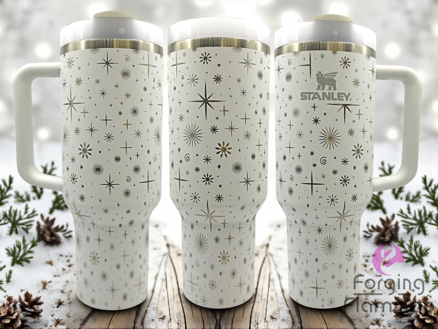 Three white Stanley tumblers with star pattern on a wooden surface with a snowy background.