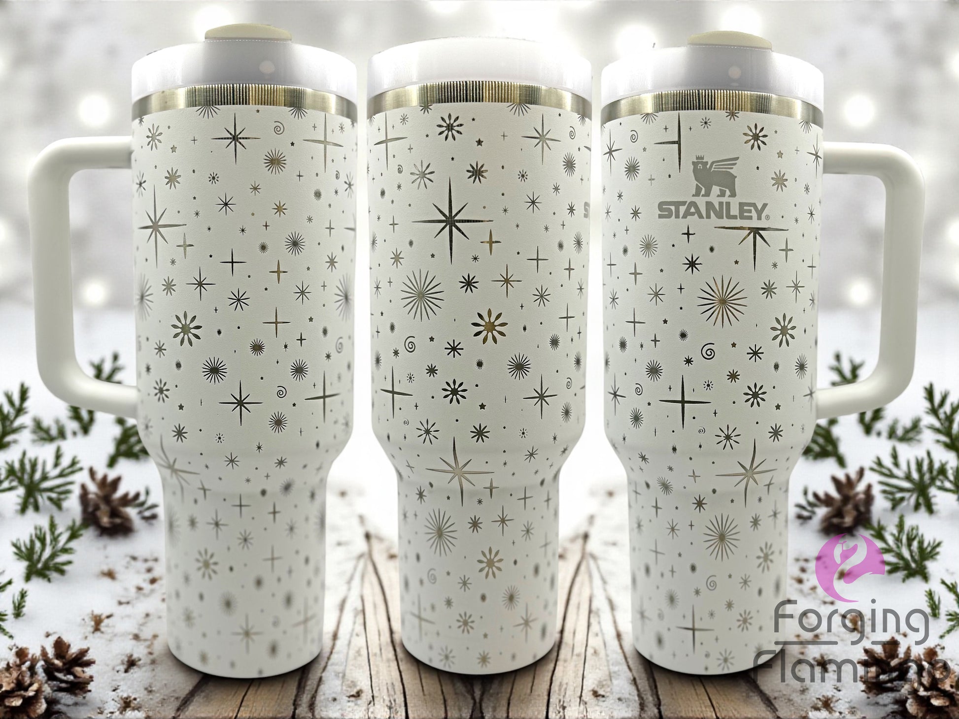Three white Stanley tumblers with star pattern on a wooden surface with a snowy background.