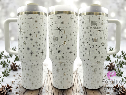 Three white Stanley tumblers with star pattern on a wooden surface with a snowy background.