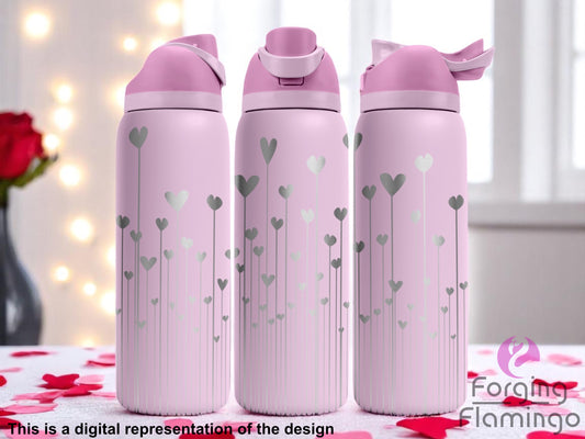 Three stainless steel tumblers with a light pink coating, featuring a laser-engraved design of tall, thin heart shapes rising vertically from the base in varying heights. The tumblers are displayed against a soft, romantic background with white curtains, glowing lights, and red rose petals scattered on the surface. Text at the bottom reads “This is a digital representation of t
