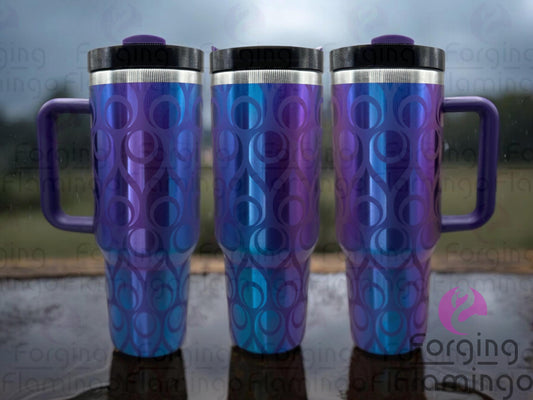 Composite image of a 40oz prism tumbler with blue and purple tones, engraved to reveal a shiny metal base that reflects the same vibrant colors. Featuring Forging Flamingo's Atomic Teardrop design, shown from multiple angles to highlight retro teardrop shapes and starbursts in a seamless wrap. Part of our Bargain Bin collection.