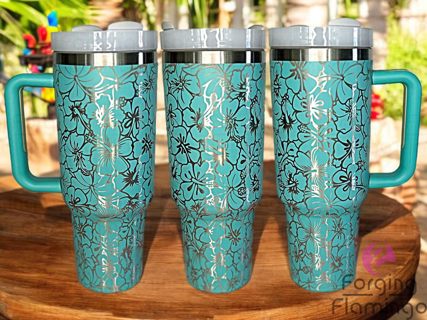 Composite image of a teal Stanley tumbler engraved with Forging Flamingo's Hibiscus Flowers design on a stainless base, shown from multiple angles to highlight the tropical floral wrap with bold hibiscus blooms.